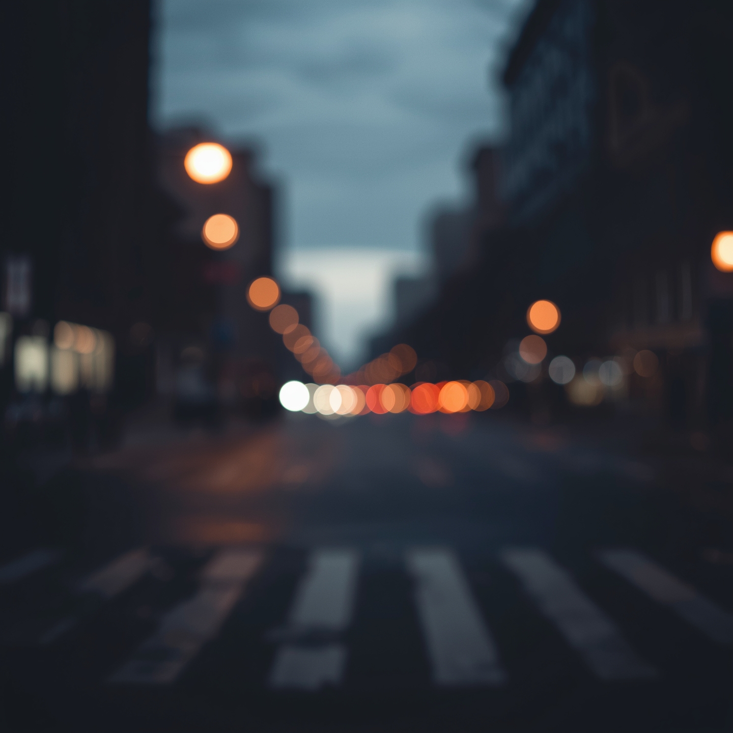 Out-of-focus city street at dusk with blurred lights and empty crosswalk.